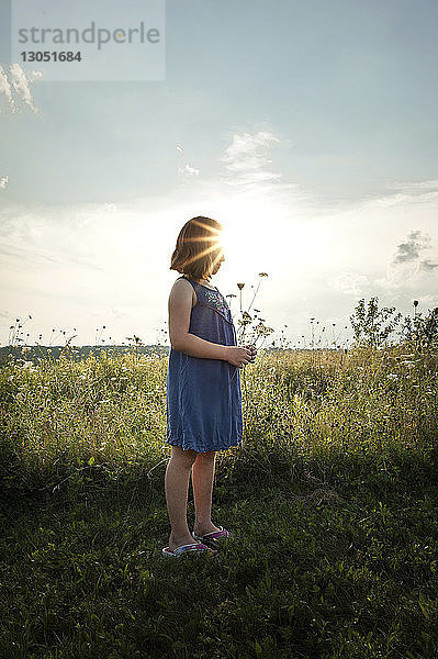 Mädchen hält Blume  während sie auf Grasfeld gegen den Himmel steht