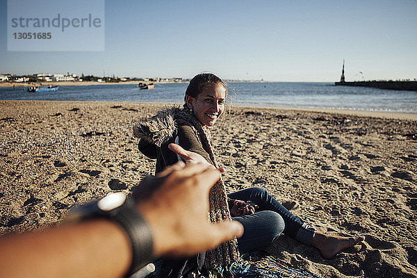 Ausgeschnittenes Bild einer Frau  die die Hand eines Mannes hält  während sie am Strand im Sand sitzt