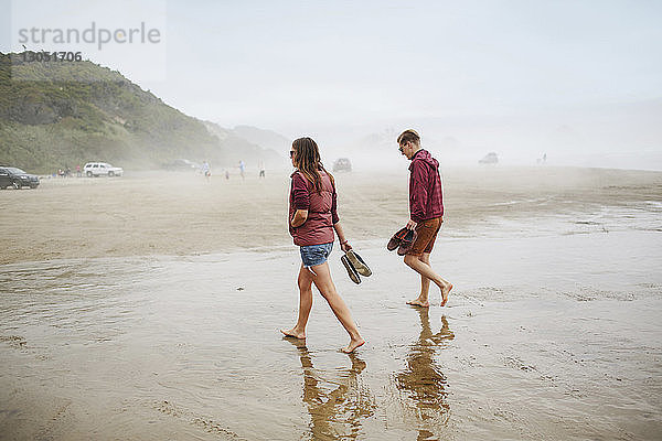 Paar hält Schuhe beim Strandspaziergang im Urlaub