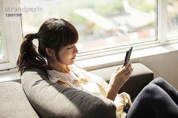 Seitenansicht einer Geschäftsfrau  die ein Smartphone auf dem Sofa im Kreativbüro benutzt