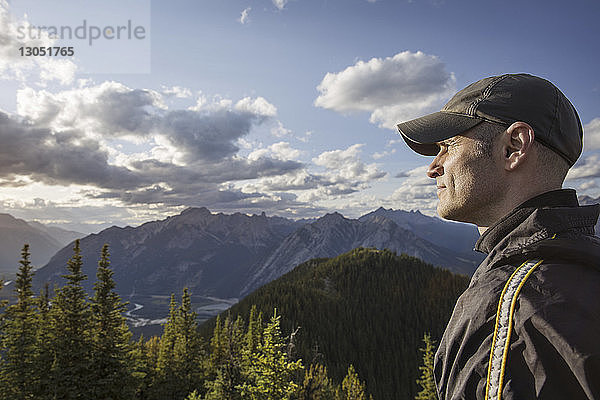 Seitenansicht eines Mannes  der wegschaut  während er im Banff-Nationalpark auf einem Berg gegen den Himmel steht