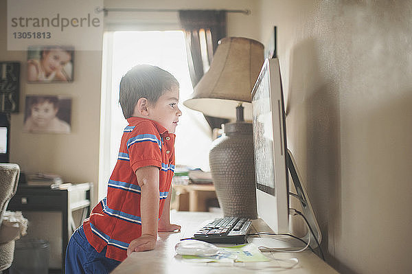 Junge schaut auf Desktop-Computer  während er zu Hause am Tisch steht