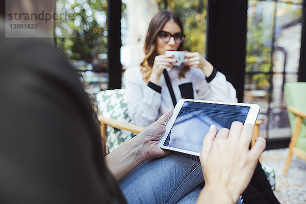 Mittelsektion einer Frau  die einen Tablet-Computer benutzt  während ein Kollege im Café Kaffee trinkt