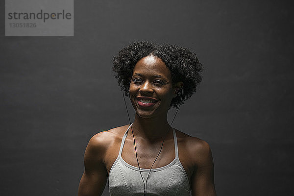 Porträt einer fröhlichen Frau  die Musik hört  während sie im Fitnessstudio an der Wand trainiert