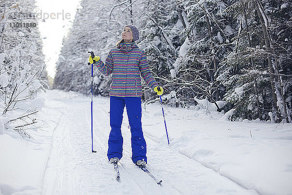 Frau mit Skiausrüstung schaut auf  während sie auf einem schneebedeckten Feld steht