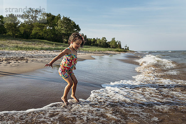 Verspieltes Mädchen springt in Wellen am Strand gegen den Himmel