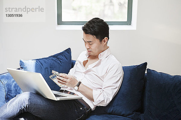 Geschäftsmann nutzt Smartphone  während er mit Laptop auf dem Sofa im Kreativbüro sitzt