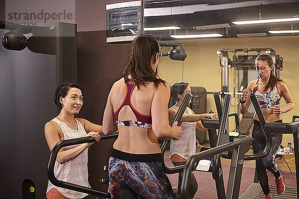 Lächelnde Frau betrachtet Freundin  die im Fitnessstudio auf dem Laufband vor dem Spiegel läuft
