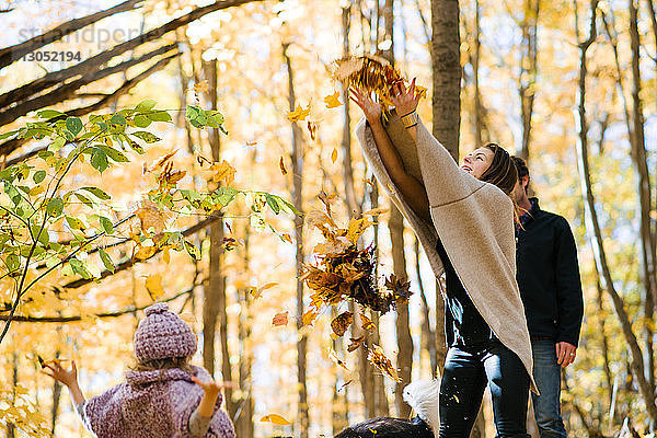 Mutter und Tochter werfen Herbstblätter im Wald in die Luft