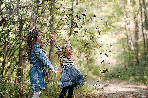 Schwestern werfen im Wald Blätter in die Luft