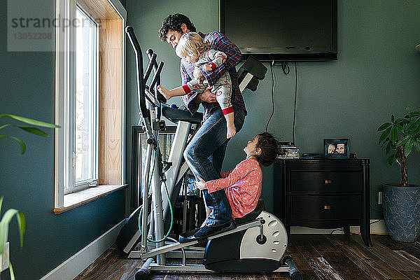 Vater und Kinder spielen auf einer elliptischen Maschine