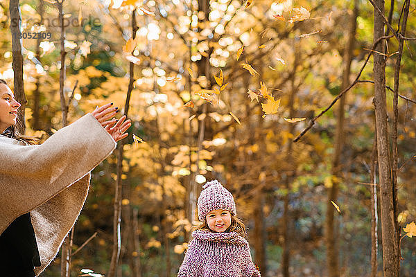 Mutter und Tochter werfen Herbstblätter im Wald in die Luft