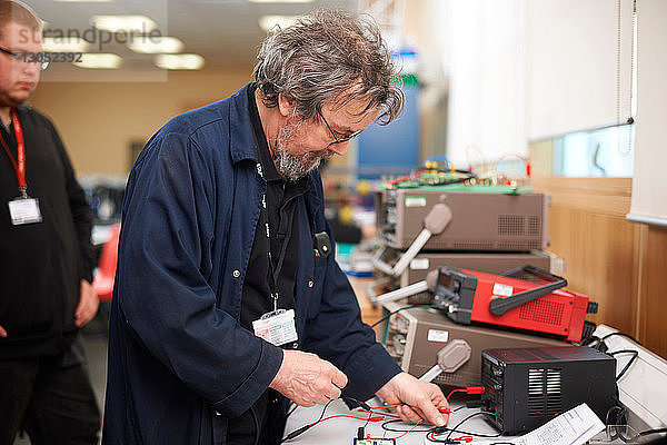 Dozent bereitet elektrisches Instrument vor  Student im Hintergrund