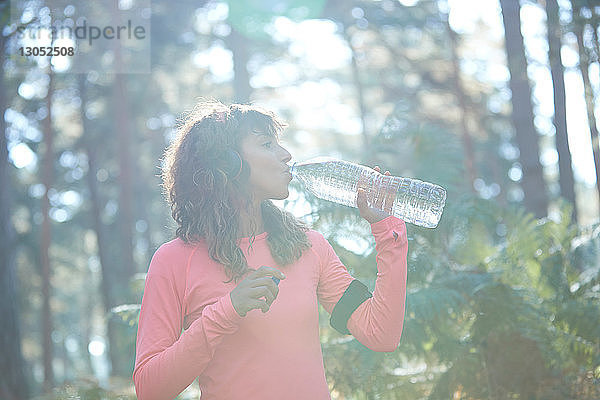 Junge weibliche Läuferin trinkt Flaschenwasser im sonnenbeschienenen Wald