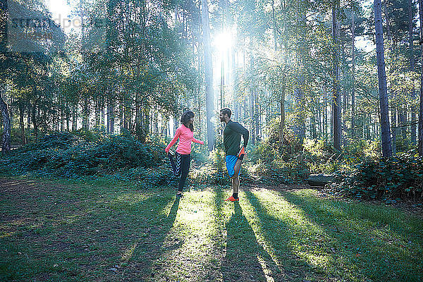 Männliche und weibliche Läufer beim Beinstrecken und Aufwärmen im sonnenbeschienenen Wald