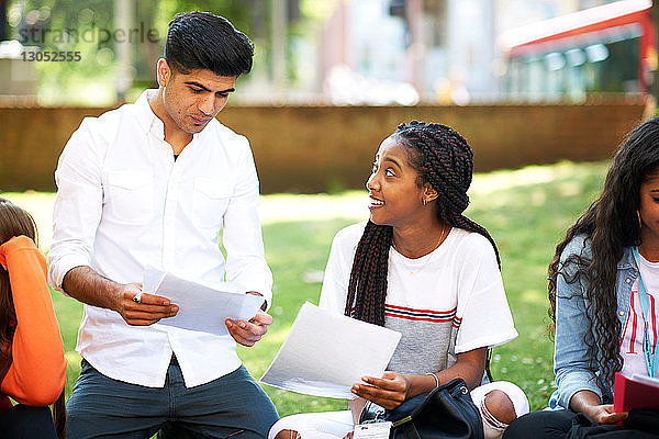 Weibliche und männliche Hochschulstudenten diskutieren über Papierkram auf dem Rasen des College-Campus