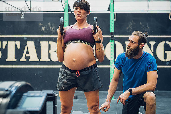 Trainerin führt schwangere Frau bei der Verwendung von Gewichten im Fitness-Studio