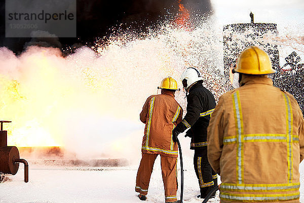 Ausbildung von Feuerwehrleuten  Team von Feuerwehrleuten  die Feuerlöschschaum auf Feuer in der Ausbildungsstätte sprühen  Rückansicht