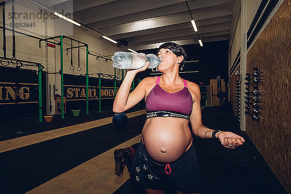 Schwangere Frau trinkt aus Wasserflasche im Fitnessstudio