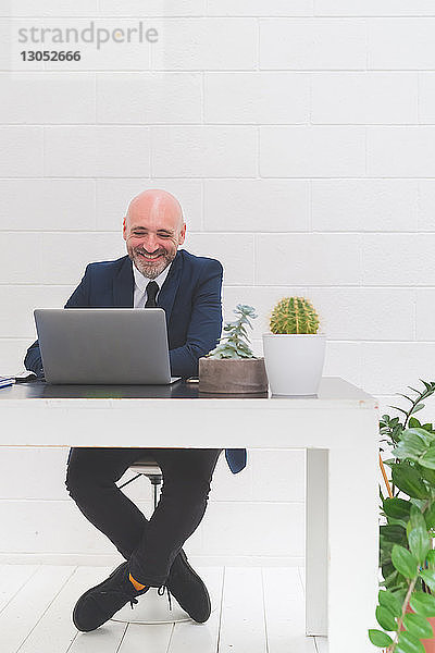 Geschäftsmann lacht  während er auf den Laptop auf dem Bürotisch schaut