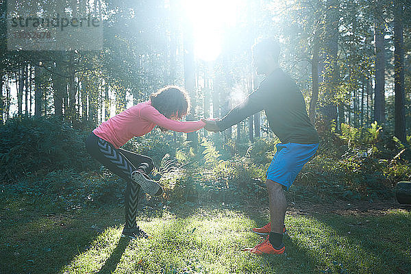 Männliche und weibliche Läufer beim Beinstrecken und Aufwärmen im sonnenbeschienenen Wald