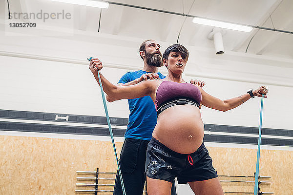 Trainerin  die schwangere Frau bei der Benutzung von Seilen im Fitnessstudio führt