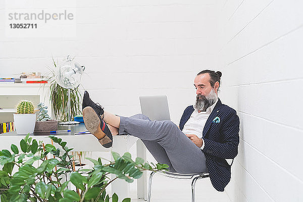 Cooler Geschäftsmann mit den Füßen im Büro  der auf den Laptop schaut