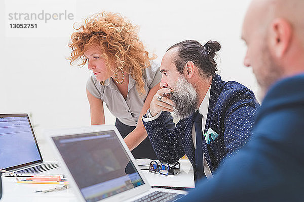 Geschäftsfrau und Männer schauen auf den Laptop auf dem Bürotisch  Blick über die Schulter