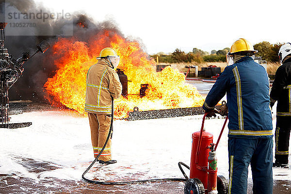 Ausbildung von Feuerwehrleuten  Team von Feuerwehrleuten  die Feuerlöschschaum auf Feuer in der Ausbildungsstätte sprühen  Rückansicht