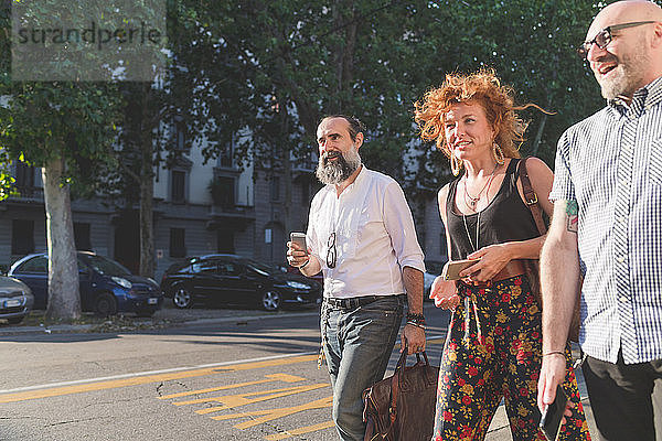 Mittelgroße erwachsene Frau und männliche Freunde unterhalten sich beim Spaziergang auf dem Bürgersteig der Stadt