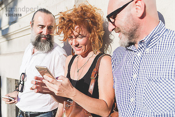 Mittelgroße erwachsene Frau und männliche Freunde lehnen an der Wand und schauen auf ein Smartphone