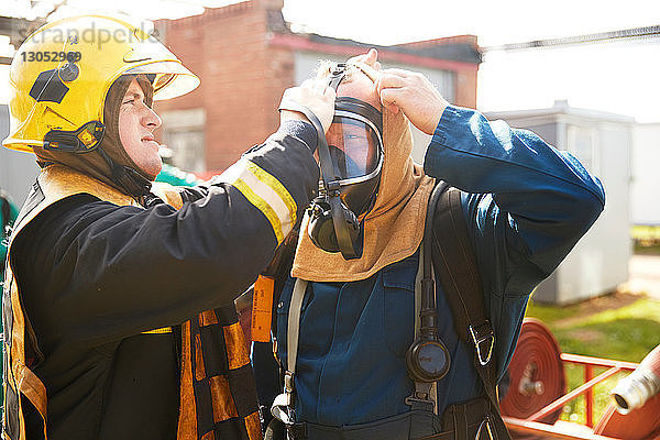 Ausbildung von Feuerwehrleuten  Vorgesetzter hilft Feuerwehrmann mit Atemschutzgerät in Trainingseinrichtung