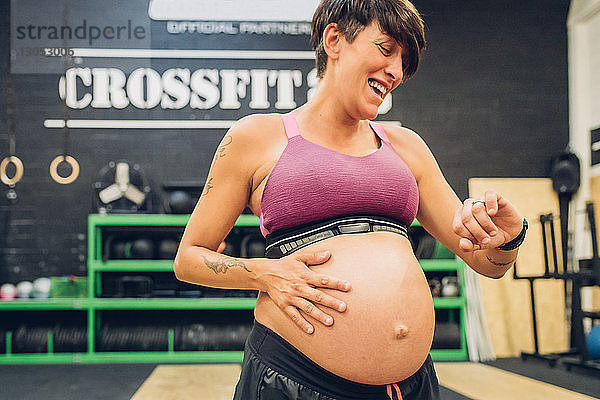 Schwangere Frau schaut auf die Zeit im Fitnessstudio