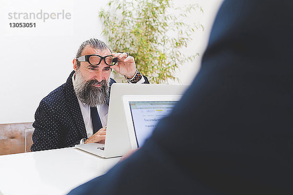 Geschäftsmann betrachtet Laptop am Büroschreibtisch  Blick über die Schulter