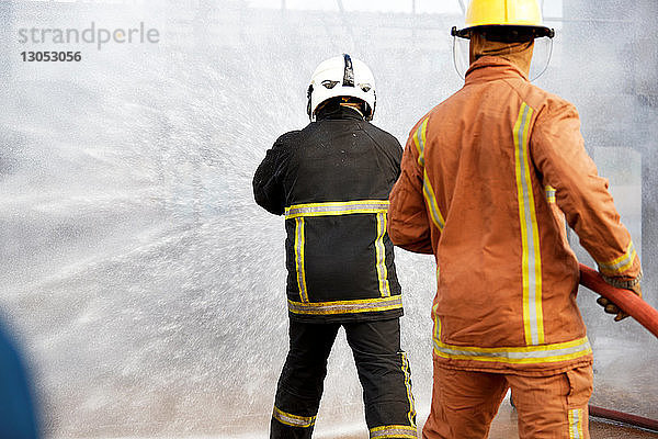 Ausbildung von Feuerwehrleuten  Feuerwehrmänner sprühen Wasser in der Trainingsanlage  Rückansicht