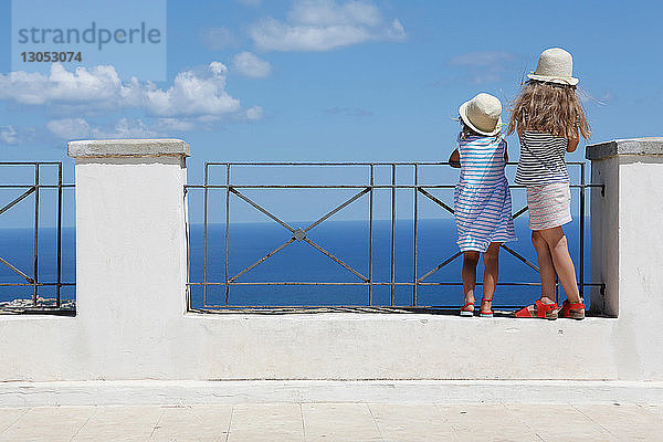 Zwei Mädchen mit Sonnenhüten blicken von der Mauer aufs Meer hinaus  Erice  Sizilien  Italien