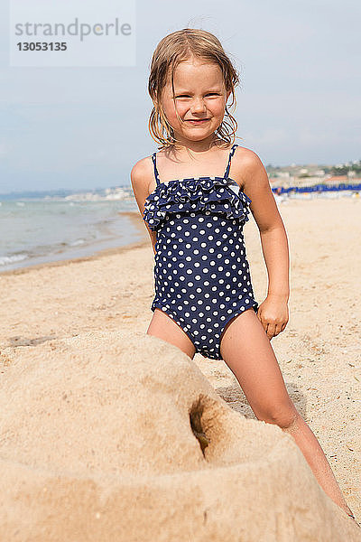 Süßes Mädchen baut Sandburg am Strand in geflecktem Badeanzug  Porträt  Castellammare del Golfo  Sizilien  Italien