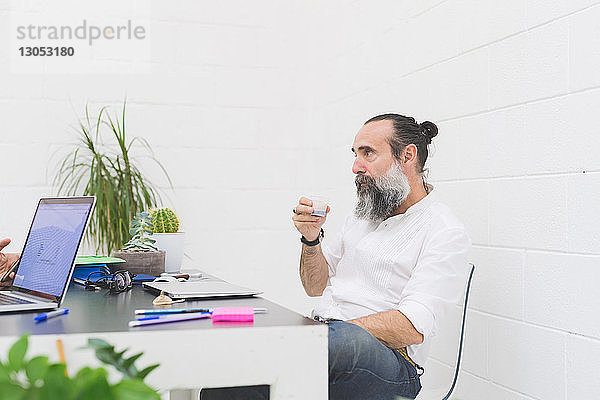 Hipster-Geschäftsmann trinkt Wasser am Bürotisch