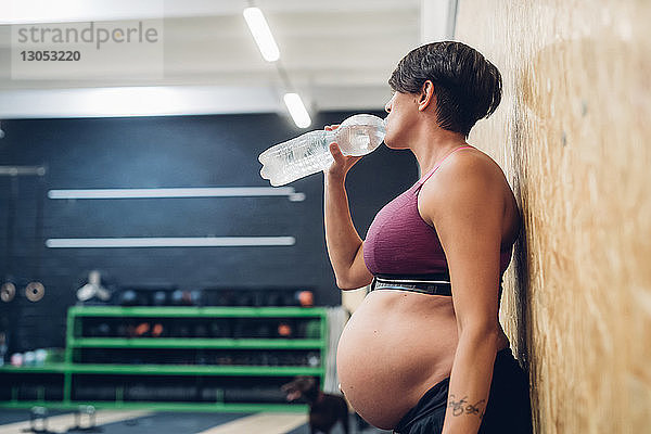 Schwangere Frau trinkt aus Wasserflasche im Fitnessstudio