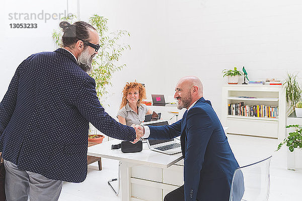 Geschäftsmann und Kunde schütteln Hände am Bürotisch