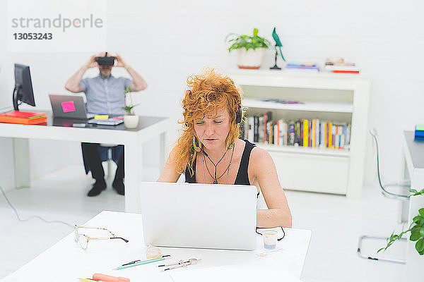 Geschäftsfrau tippt am Laptop am Büroschreibtisch und hört dabei Kopfhörer