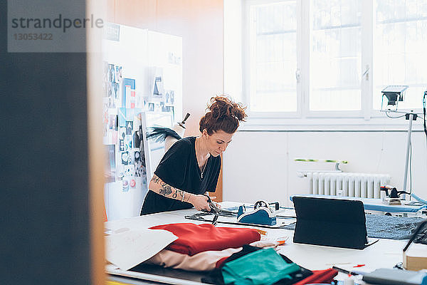 Modedesignerin schneidet Stoff nach Schnittmuster der Schneiderin