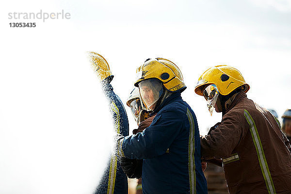 Feuerwehrmänner von Sprühwasser aus Feuerwehrschlauch bedeckt