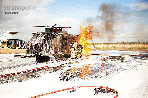 Ausbildung von Feuerwehrleuten  Team von Feuerwehrleuten sprüht Feuerlöschschaum beim Scheinfeuer eines Hubschraubers in einer Ausbildungseinrichtung