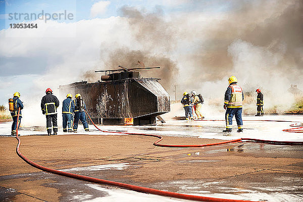 Ausbildung von Feuerwehrleuten  Team von Feuerwehrleuten sprüht Feuerlöschschaum am Scheinhelikopter in der Ausbildungsstätte