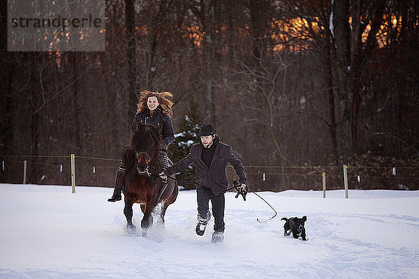 Mann hält Seil  während Frau auf schneebedecktem Feld reitet