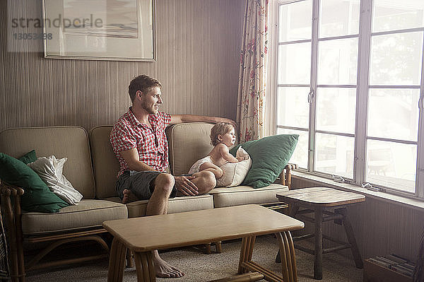 Vater und Sohn schauen durch das Fenster  während sie auf dem Sofa sitzen
