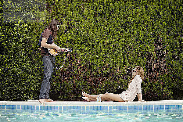 Mann spielt Mandoline  während Frau am Swimmingpool sitzt
