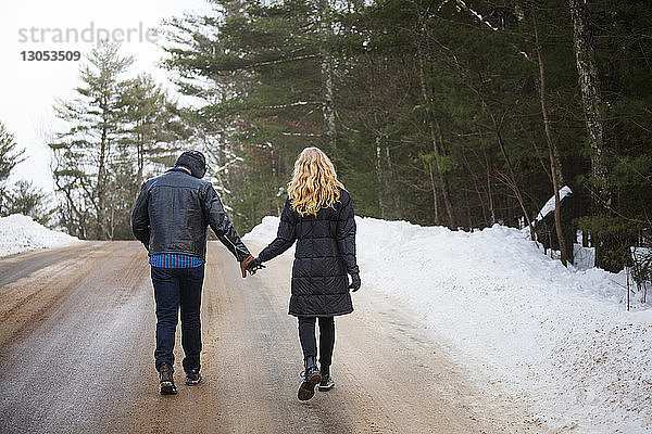 Rückansicht eines Paares  das sich beim Gehen auf der Straße an den Händen hält