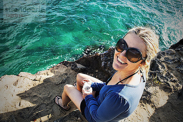 Hochwinkelansicht einer lächelnden Frau  die auf einem Felsen am Fluss sitzt